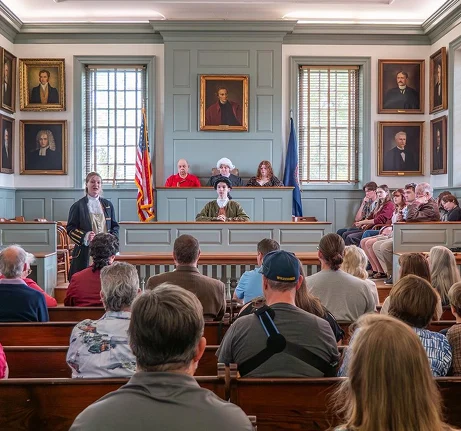A historical courtroom reenactment with people in period costumes addressing an audience.