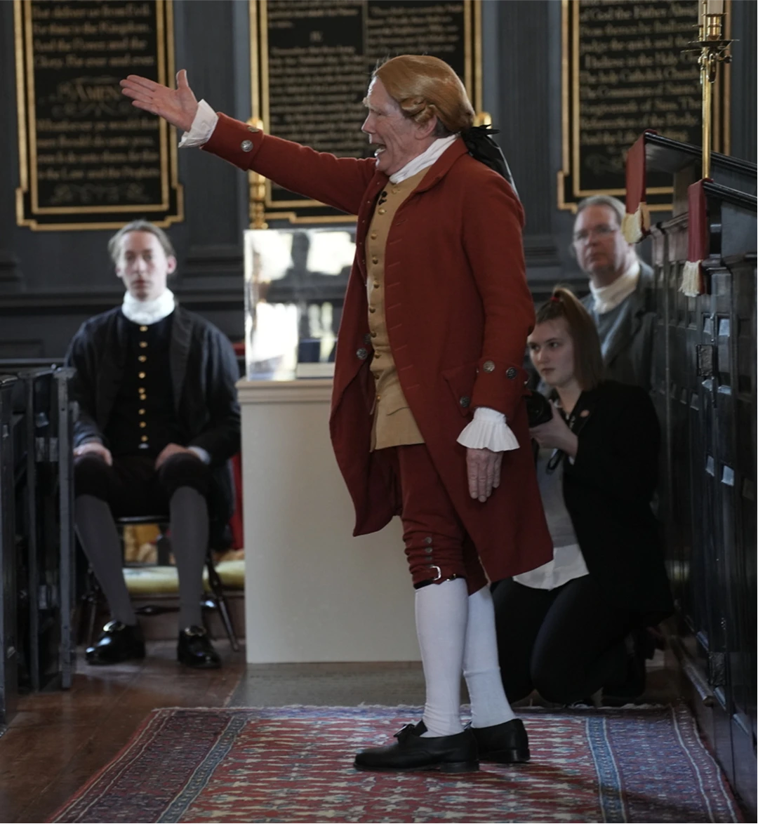 Person in colonial attire speaking with parchment in hand.